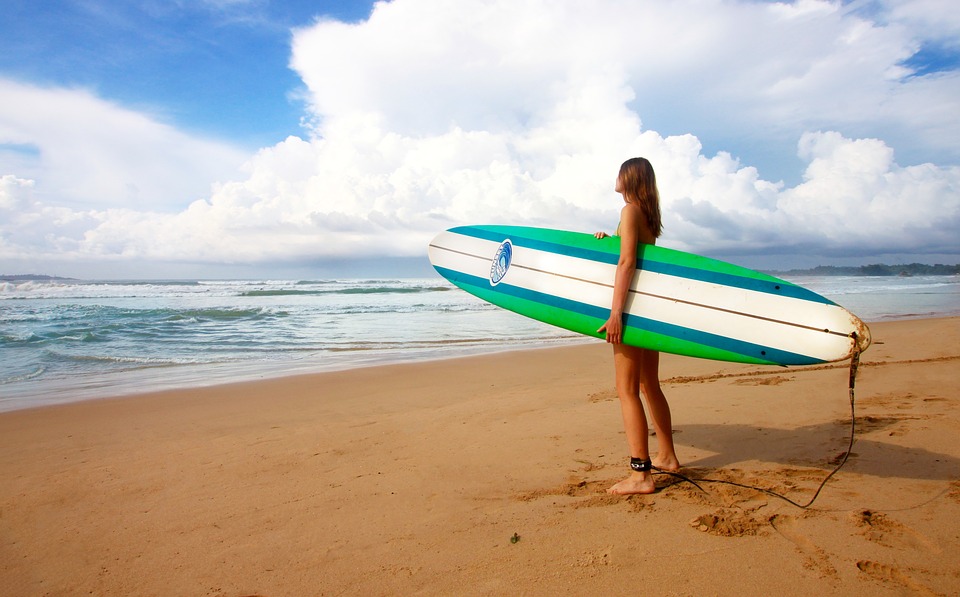 サーフボードを持った女性が海を見つめている画像